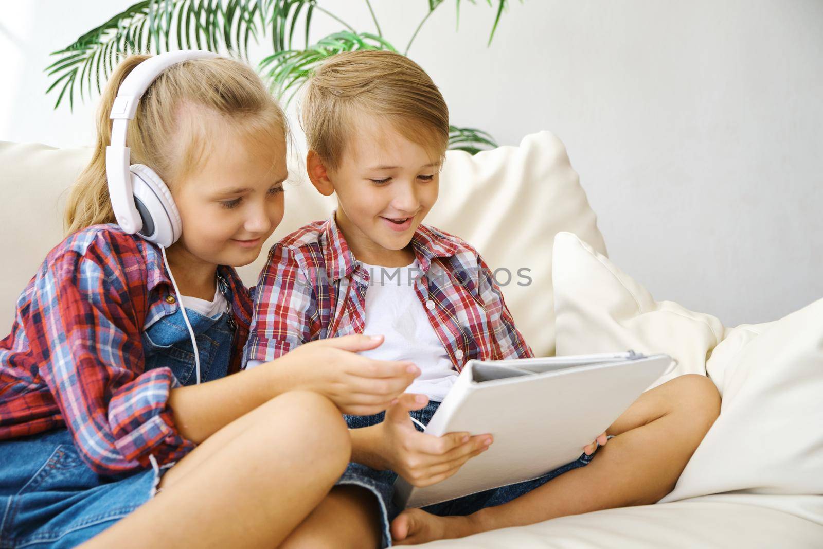 Cute brother and sister with headphones enjoying tablet at home. family, children, technology and home concept