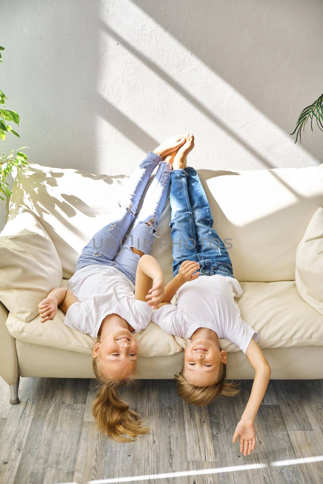 Pretty little girl and boy are lying on sofa in living room by InnaVlasova