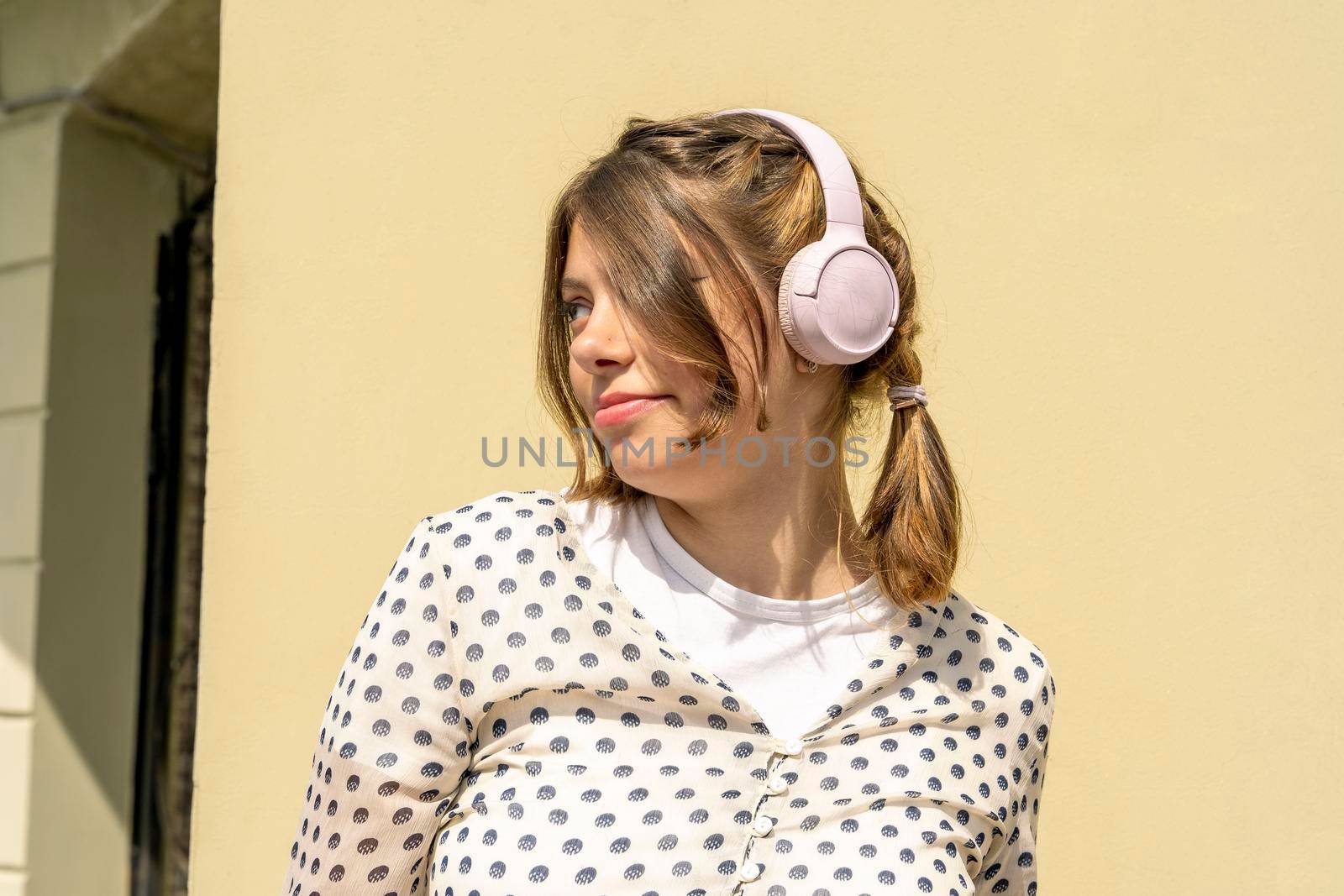 Teenage cute Caucasian girl has a good time listening to music with headphones. a beautiful fashionable girl enjoys music. a girl is dancing, listening to music with headphones, against a yellow background