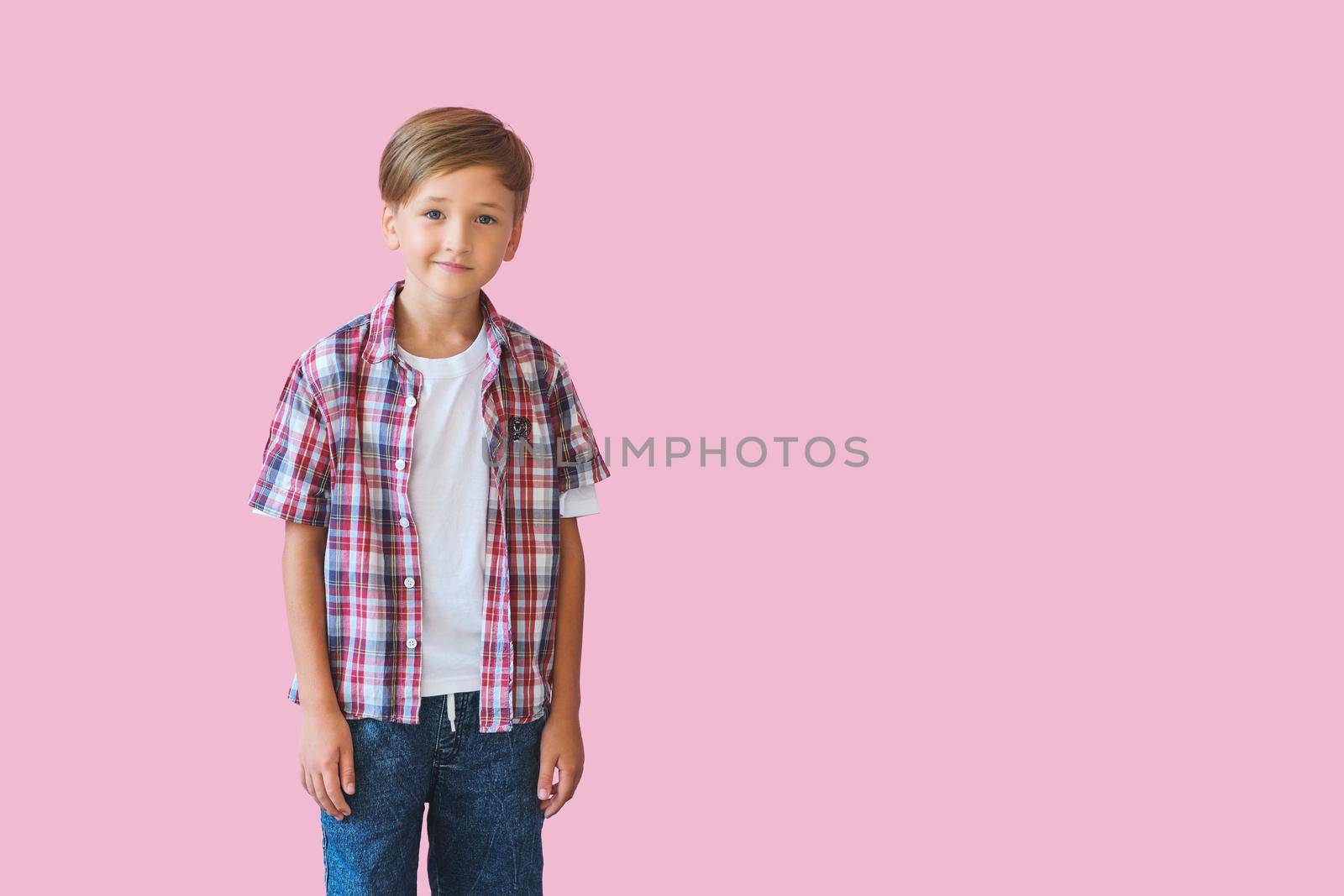 Young happy boy dressed in jeans, a white T-shirt and a plaid shirt isolated on pink background with copy space