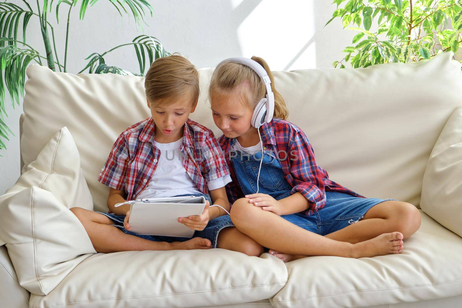 Cute brother and sister with headphones enjoying tablet at home. family, children, technology and home concept