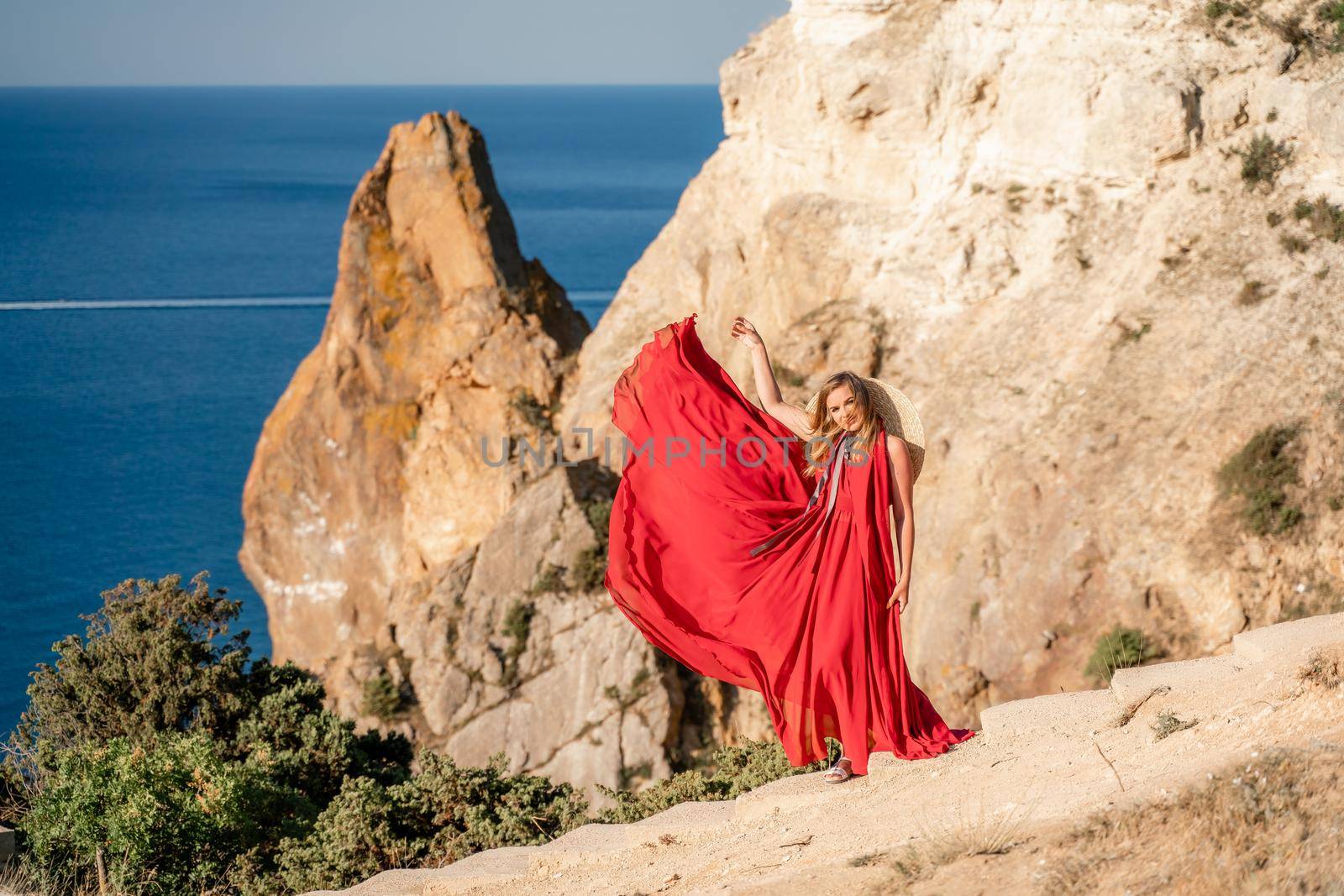 A woman in a red flying dress fluttering in the wind, against the backdrop of the sea