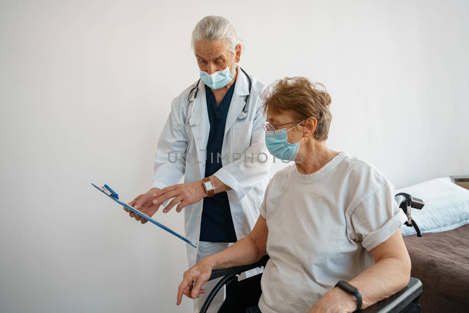 Doctor in mask explaining to a sick patient in wheelchair details of treatment. High quality photo