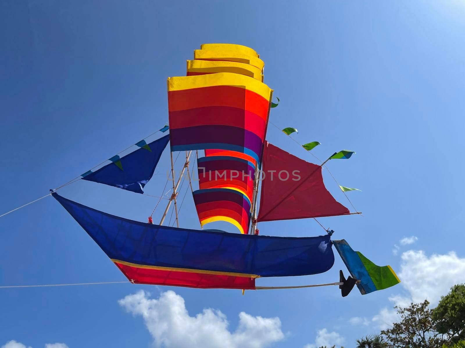 flying ship, rainbow colored ship kite flies on the blue sky and cloud in the beach