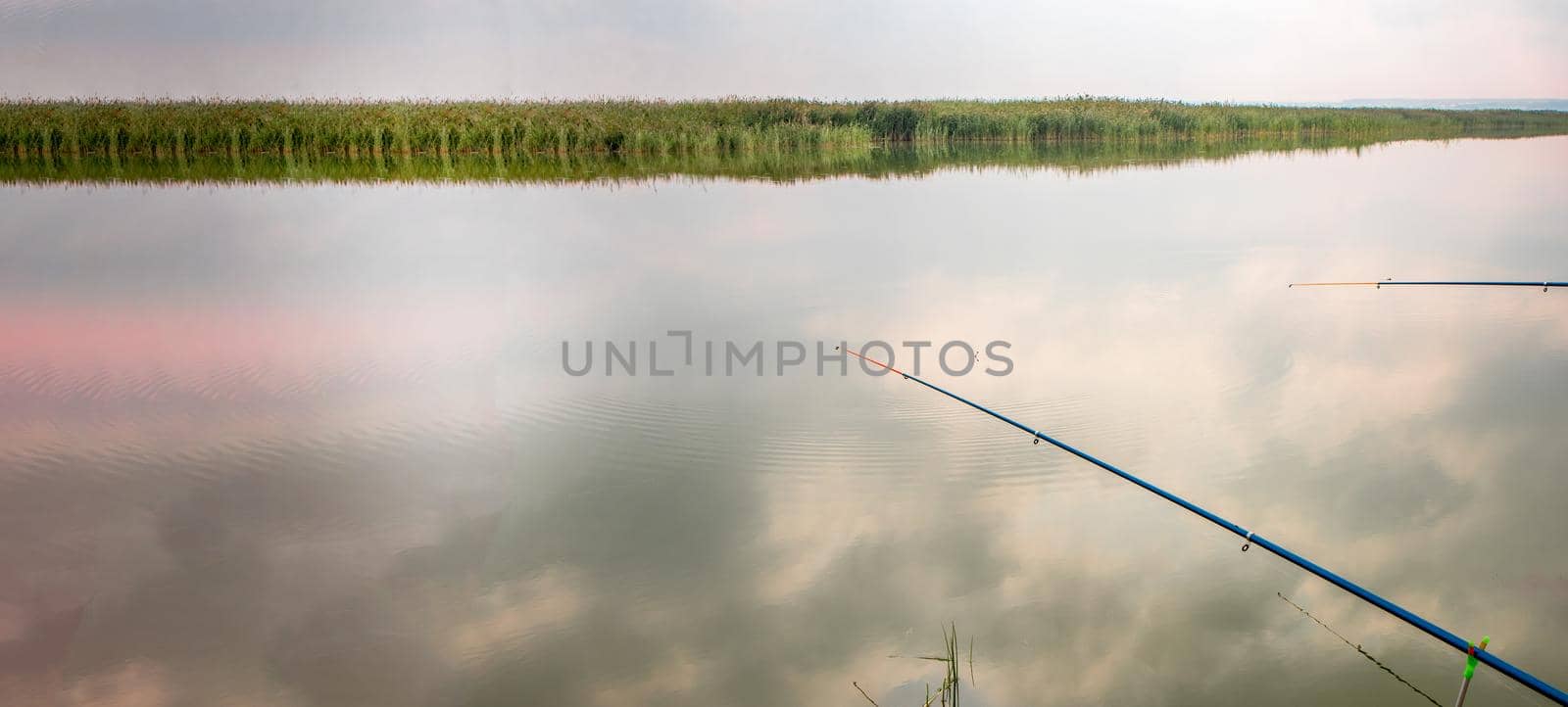 Two fishing rods reflected in the water surface, the reflection of clouds. Quiet hobby, banner.