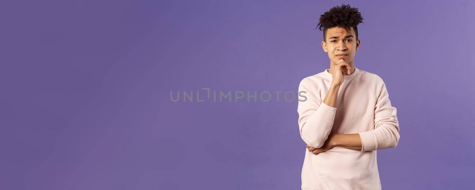 Thoughtful, skeptical young man look judgemental and hesitant at camera while pondering between choices, consider what to do, thinking over purple background, solving troublesome situation by Benzoix