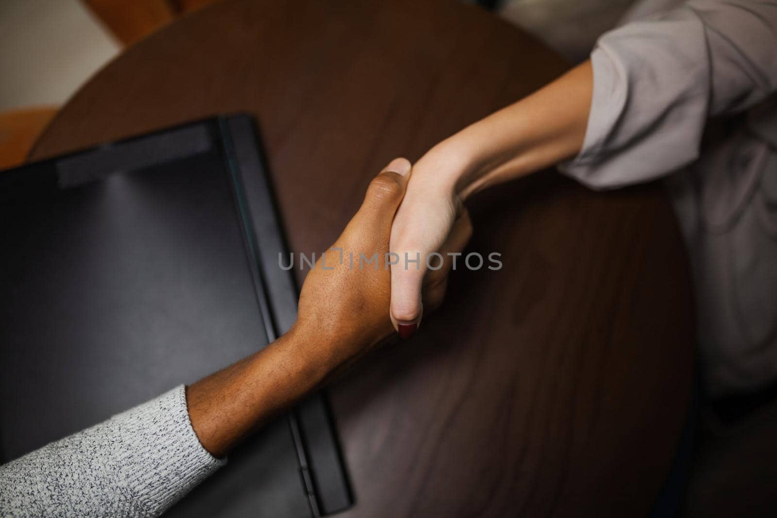 Two multiracial business colleagues working after work or during coffee break in a restaurant. Man and woman shaking hands after successful meeting.. by kokimk