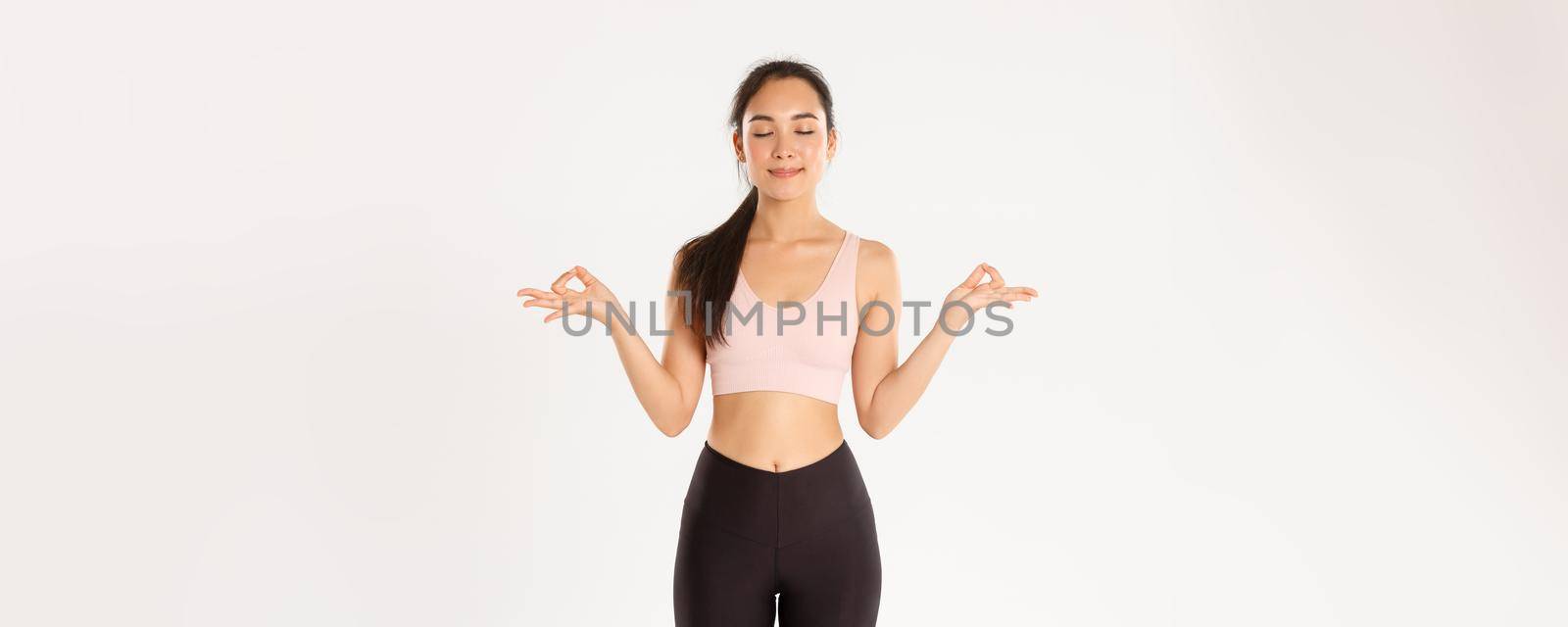 Sport, wellbeing and active lifestyle concept. Smiling calm and relaxed fitness girl, woman in sportswear close eyes and standing in lotus pose, reach nirvana on yoga classes, meditating.