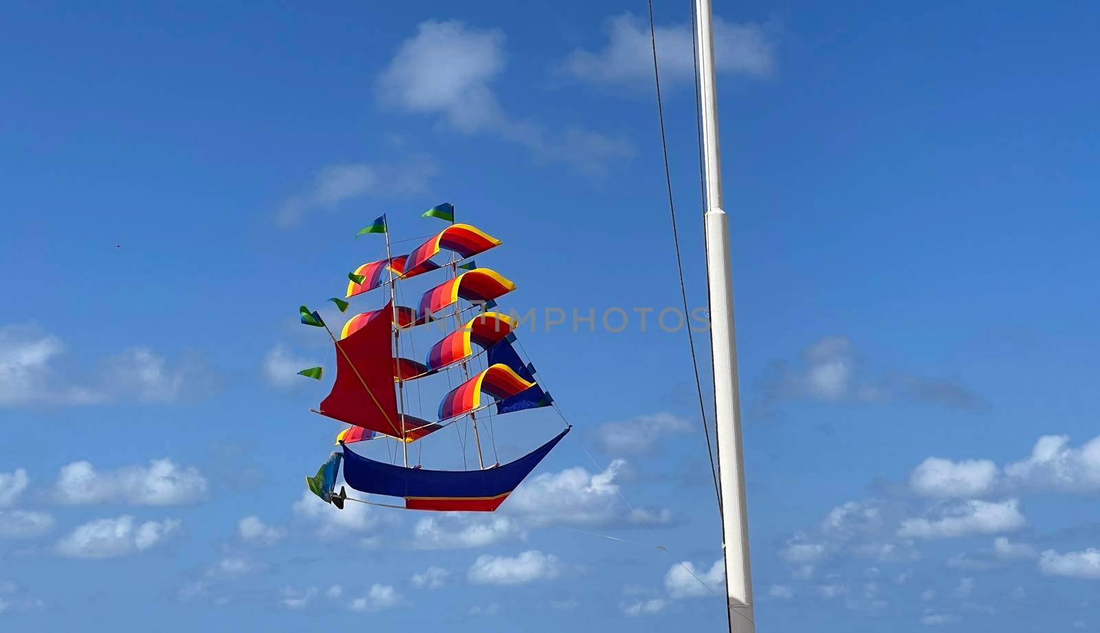 flying ship, rainbow colored ship kite flies on the blue sky and cloud in the beach