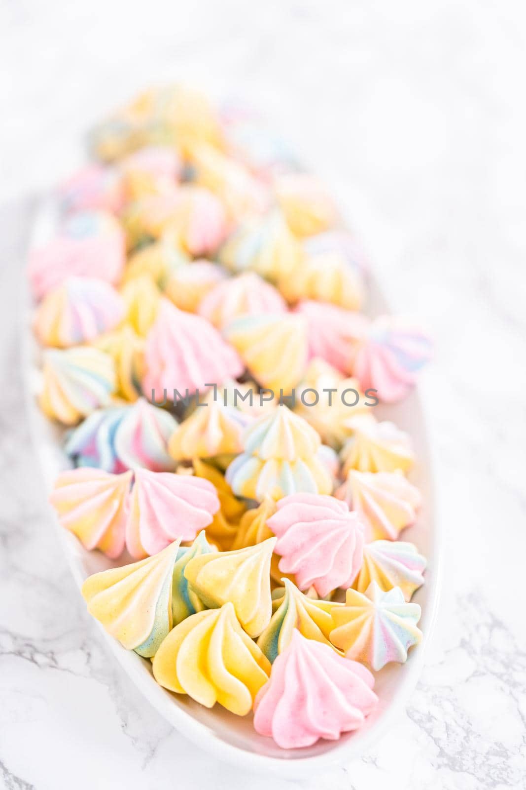 Multicolored unicorn meringue cookies on a white serving plate.