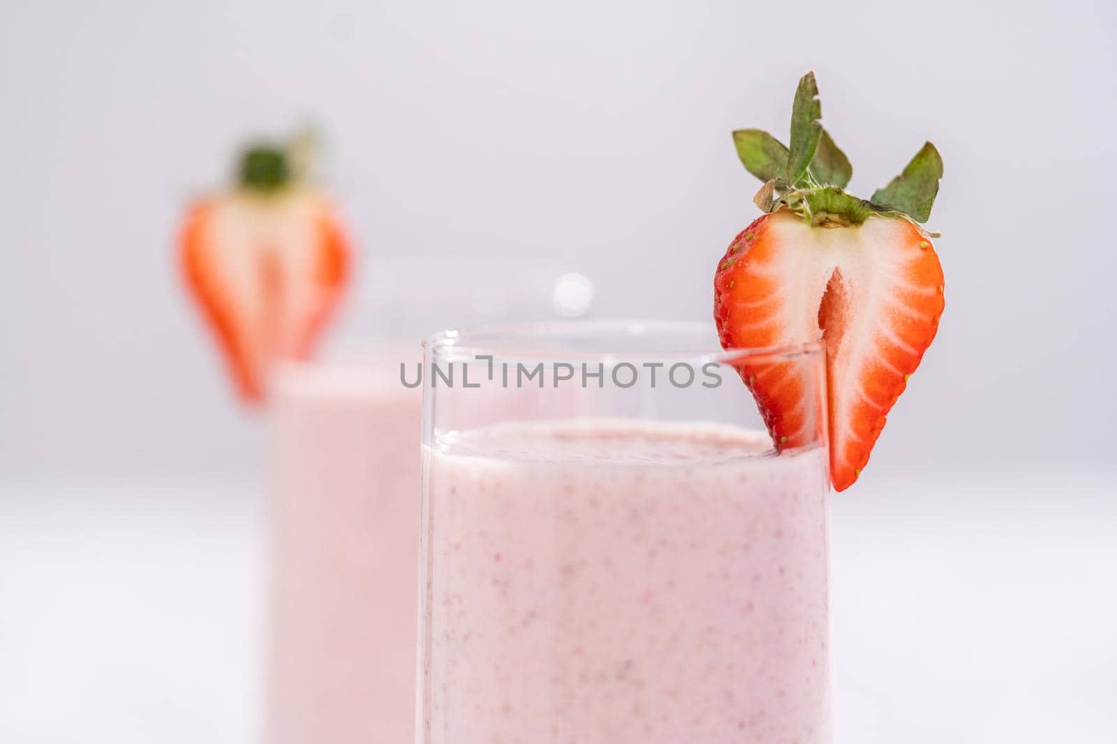 Freshly made healthy breakfast strawberry banana smoothie garnished with fresh strawberry and paper straw.