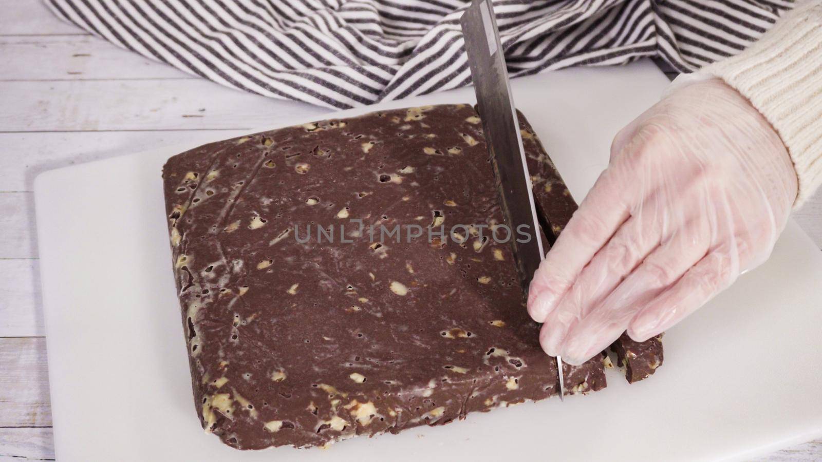 Step by step. Cutting homemade macadamia fudge on a white cutting board.