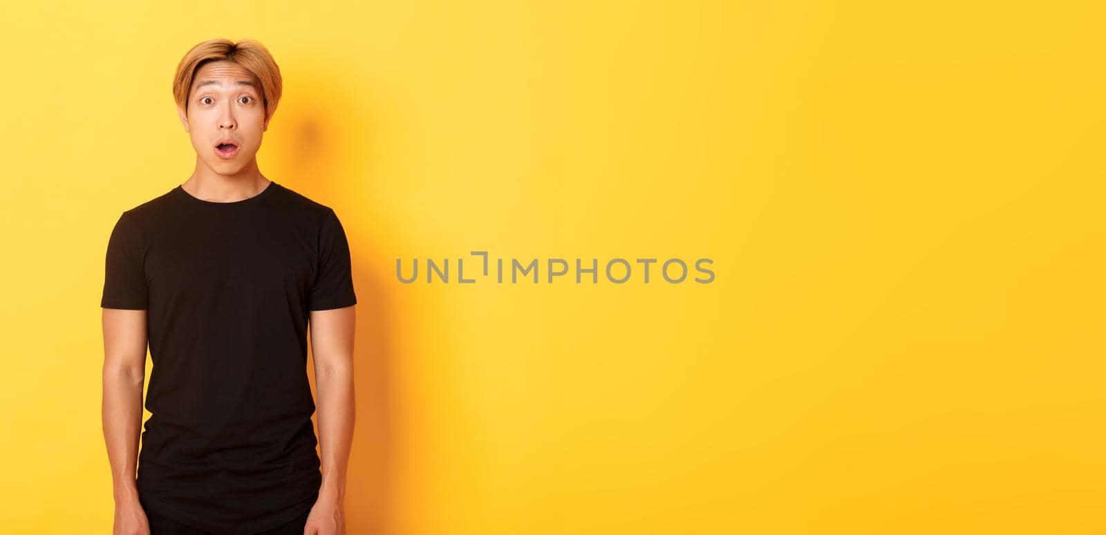 Portrait of startled handsome asian blond guy, drop jaw and gasping impressed, yellow background by Benzoix