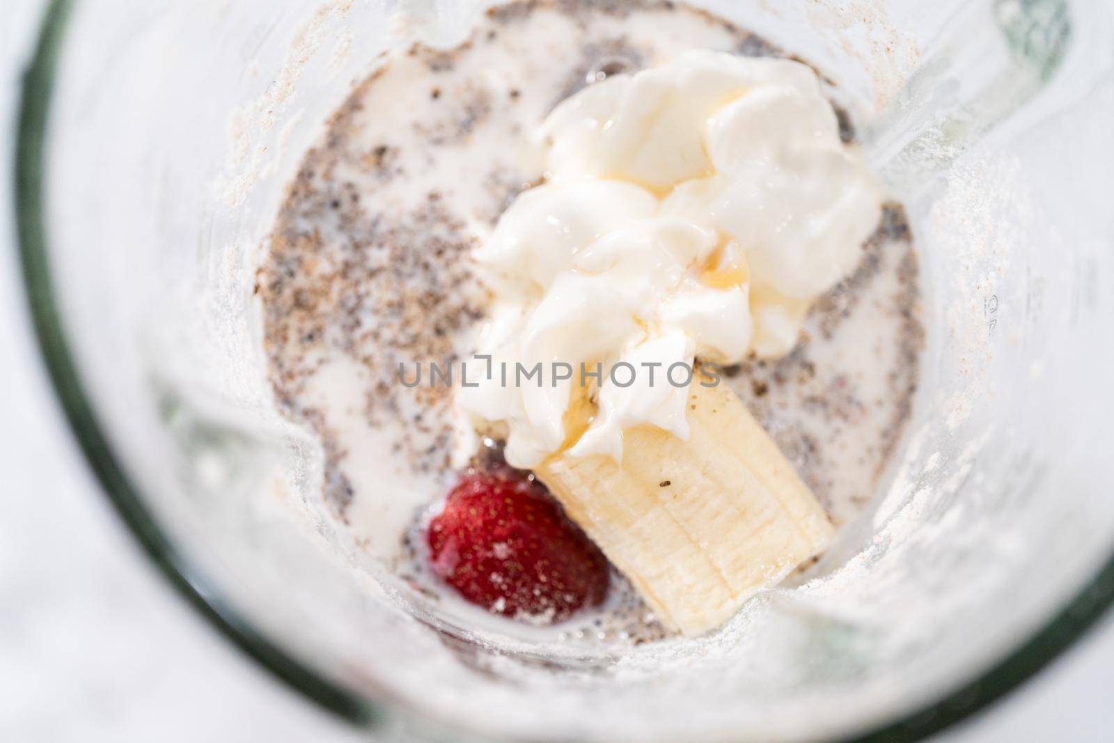 Blending ingredients for healthy breakfast strawberry banana smoothie in a kitchen blender.