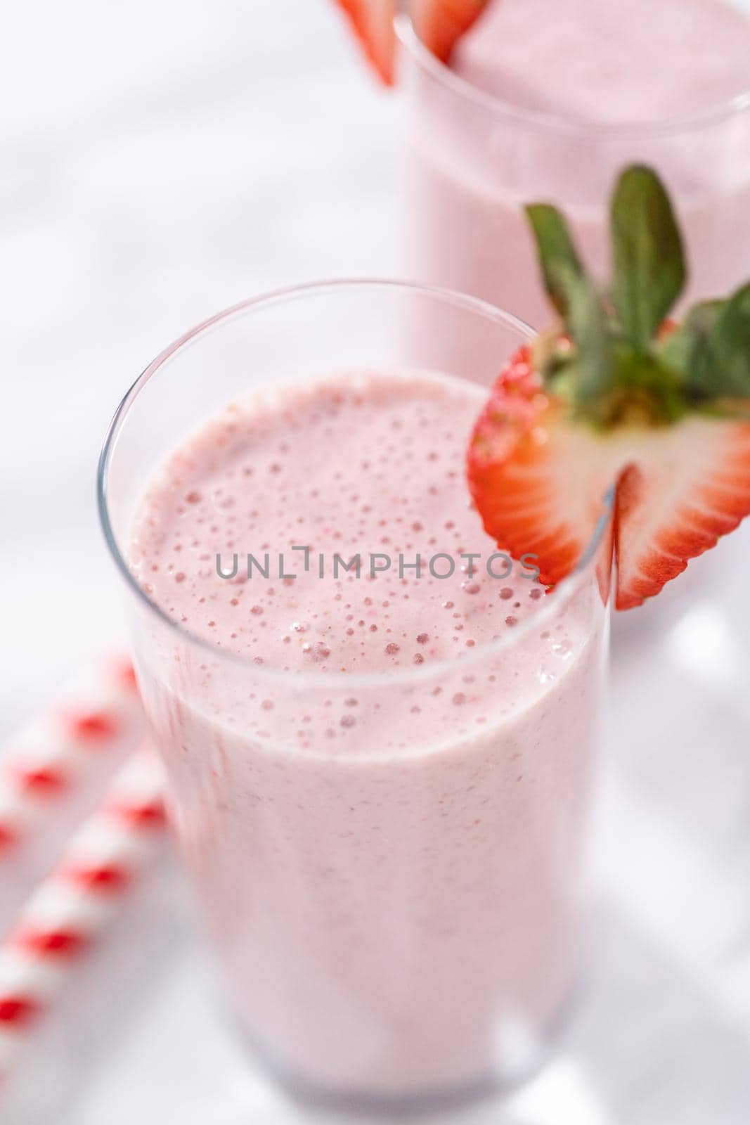 Freshly made healthy breakfast strawberry banana smoothie garnished with fresh strawberry and paper straw.