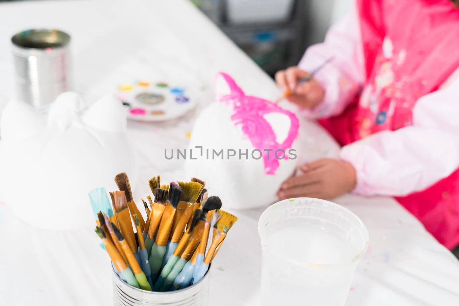 Little girl painting Halloween pumpkin with acrylic paint.