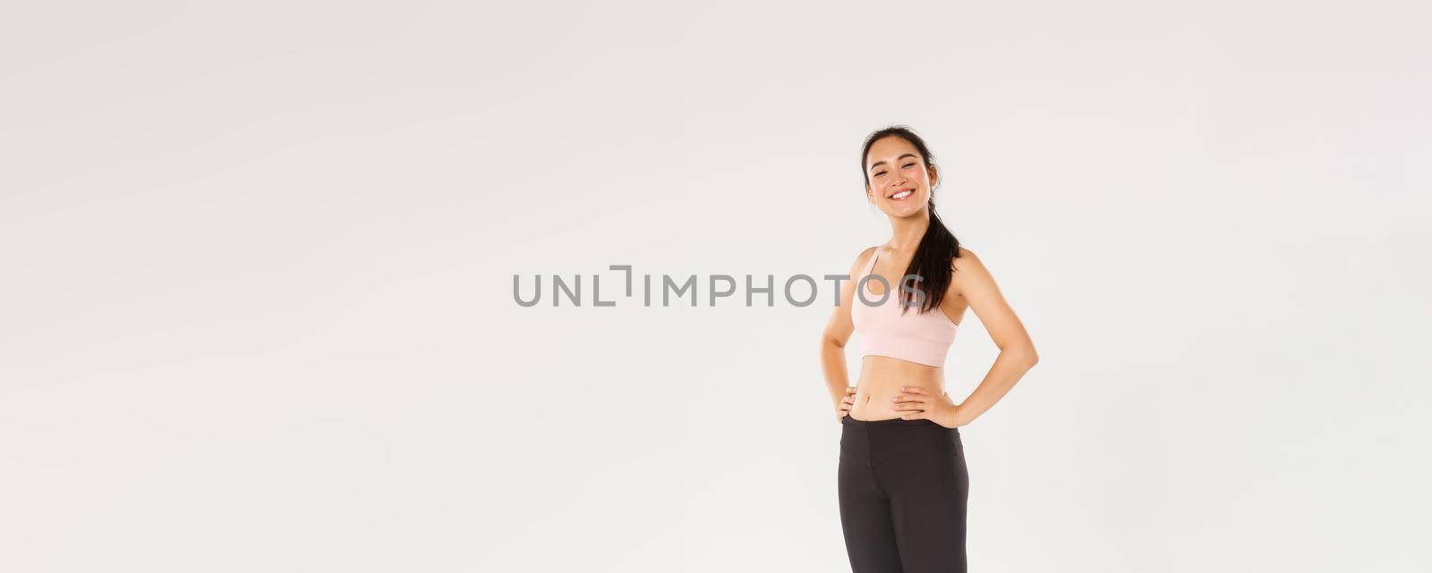Full length of proud and happy female athlete in sportswear looking happy and accomplished, fitness girl gaining her sports goal, looking delighted, workout in gym, white background.