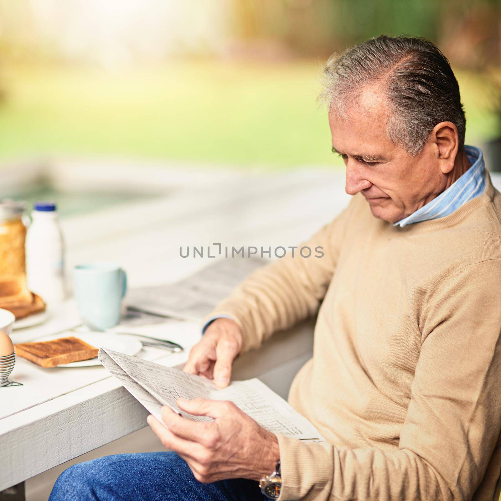 Keeping up with the news of the day. a senior man reading a newspaper with his breakfast outdoors