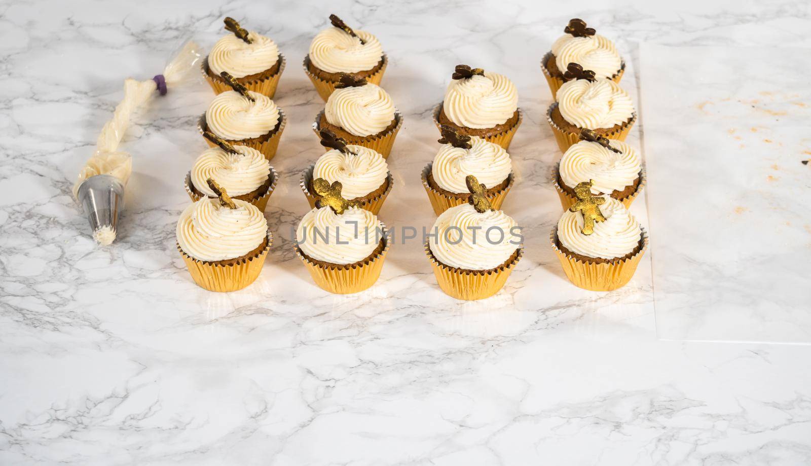 Piping eggnog buttercream frosting on top of gingerbread cupcakes and topping with a chocolate gingerbread man.