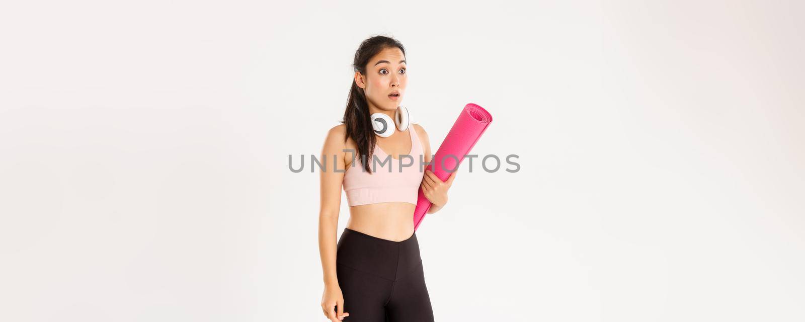 Sport, wellbeing and active lifestyle concept. Shocked asian fitness girl in stupor, drop jaw and gasping while looking left at logo or banner info, holding rubber mat for fitness exercises.