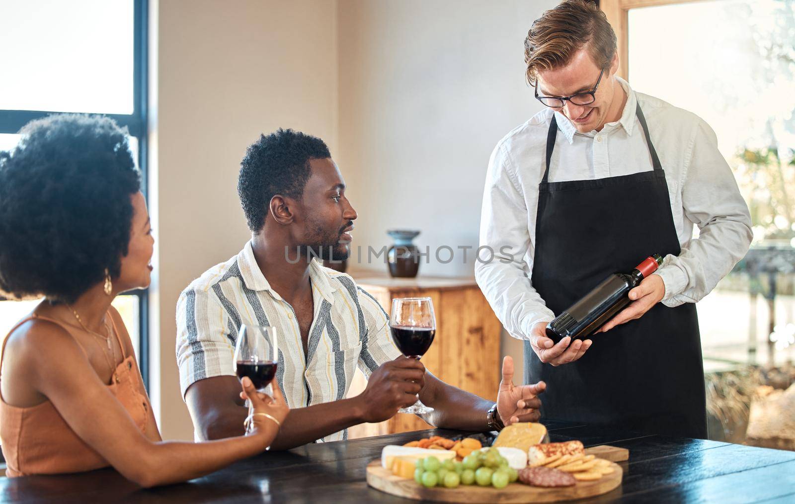 Couple doing wine tasting at a vineyard, eating food on romantic vacation and drinking alcohol at farm together. Happy African couple getting snacks from waiter at restaurant and service with smile.