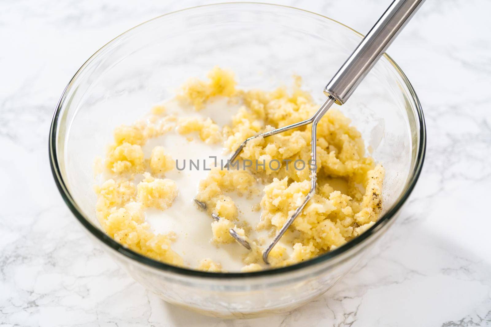 Mashed potatoes. Mashing cooked potatoes in a glass mixing bowl with a potato masher to make mashed potatoes.