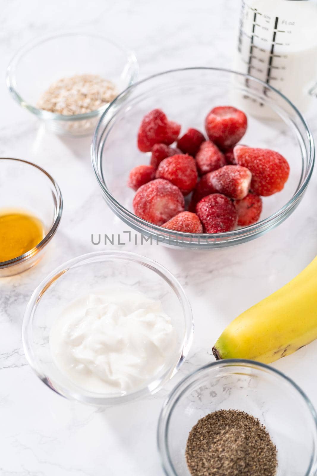Measured ingredients in a glass mixing bowl to prepare a strawberry banana smoothie.