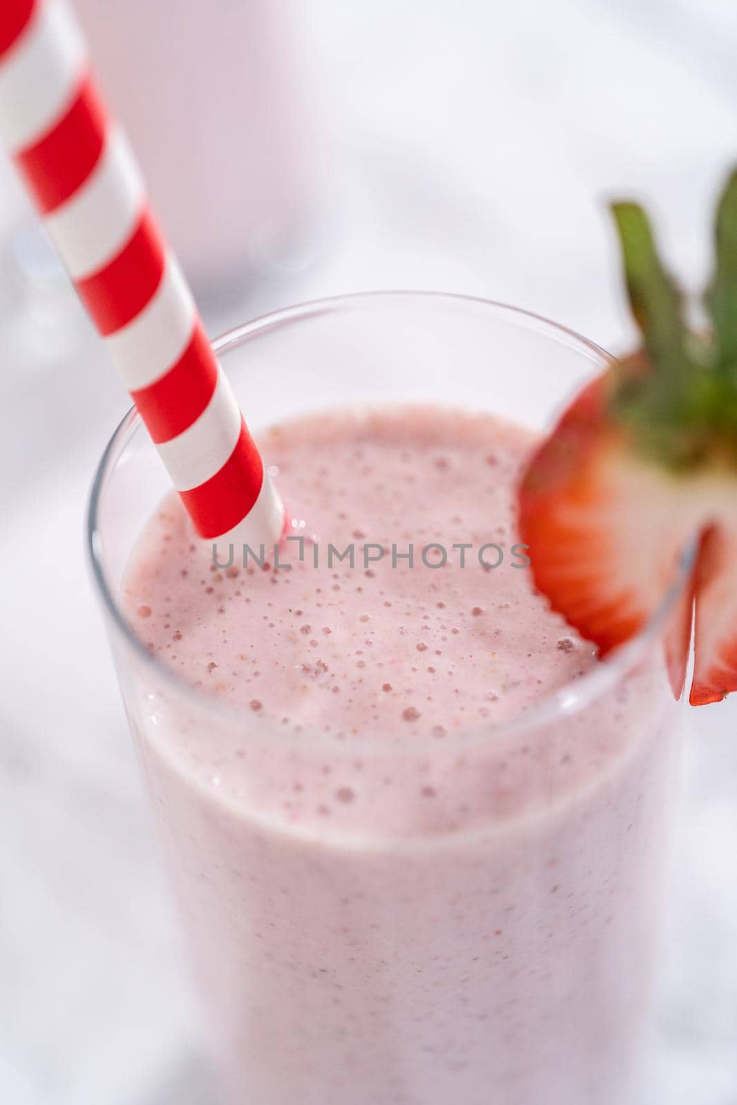 Freshly made healthy breakfast strawberry banana smoothie garnished with fresh strawberry and paper straw.