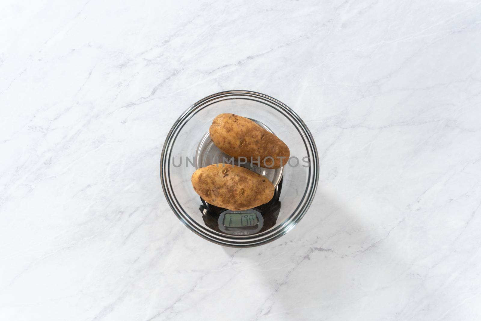 Flat lay. Pressure Cooker Baked Potatoes. Measuring raw potatoes in a glass mixing bowl on the kitchen scale.