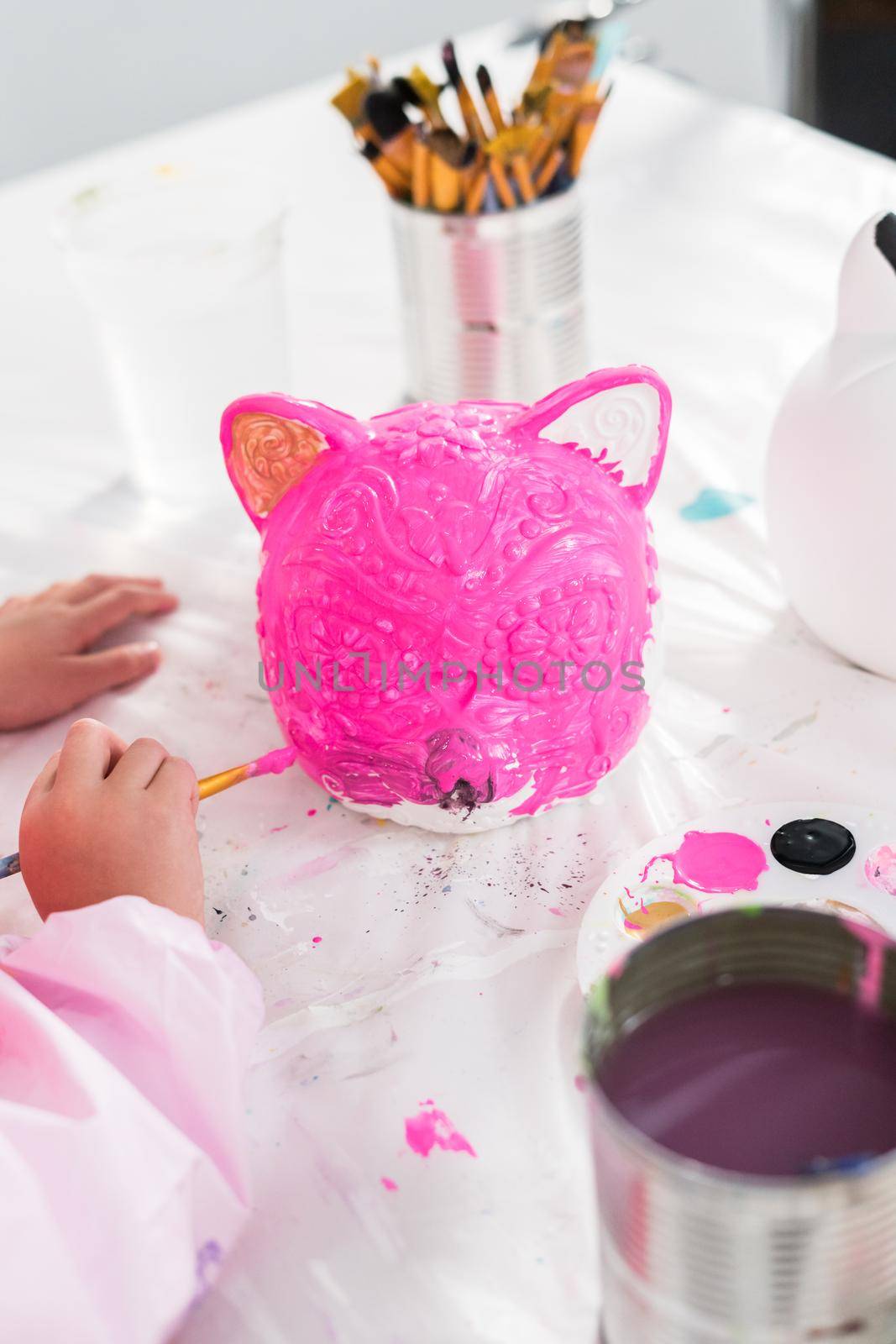 Little girl painting Halloween pumpkin with acrylic paint.