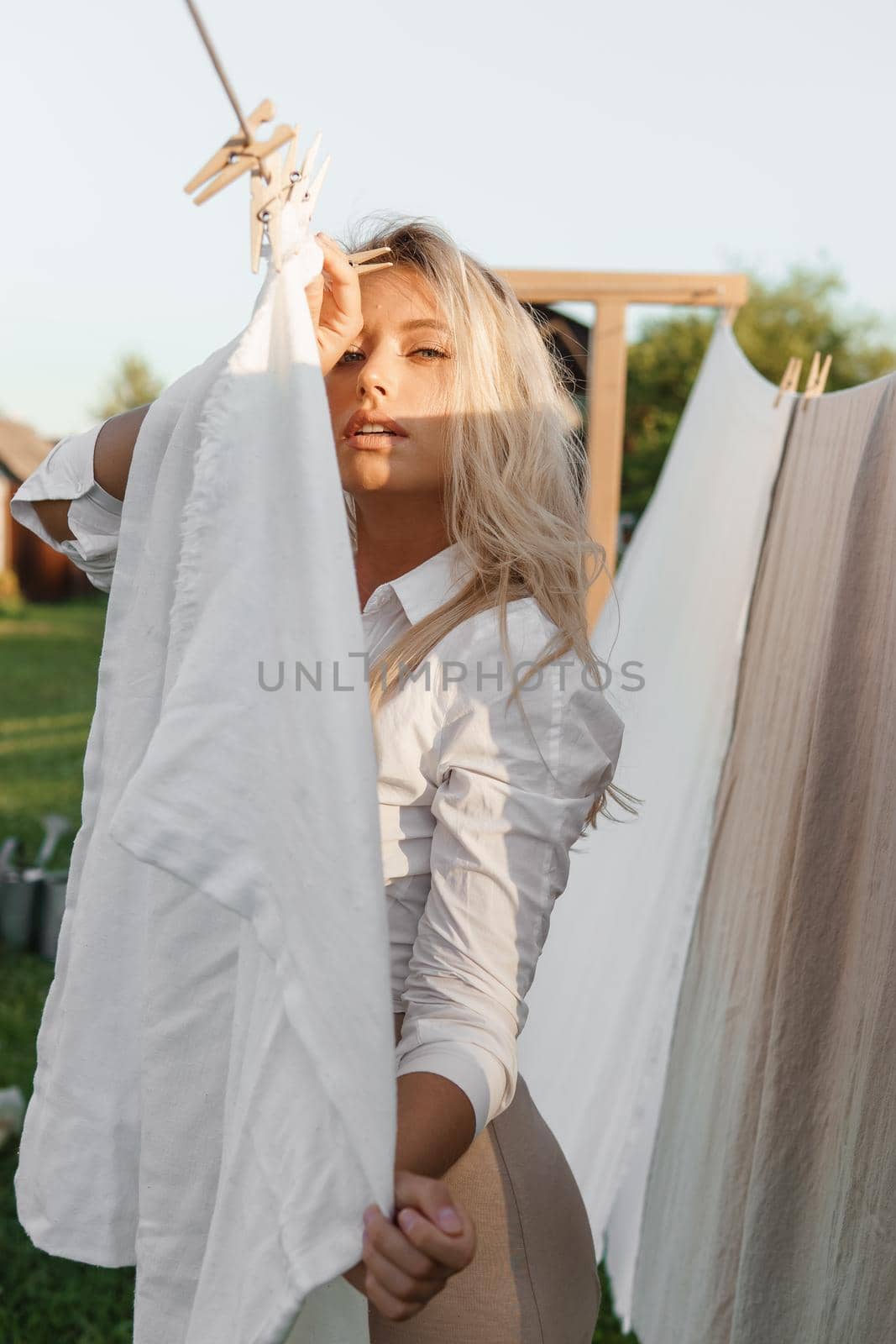 Laundry day. A woman hangs linen and towels on a tree in the courtyard of a village house. Summer cottage concept.