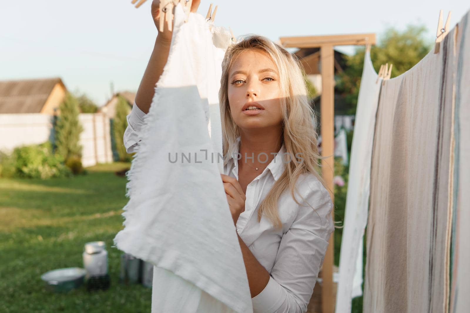 Laundry day. A woman hangs linen and towels on a tree in the courtyard of a village house. Summer cottage concept.