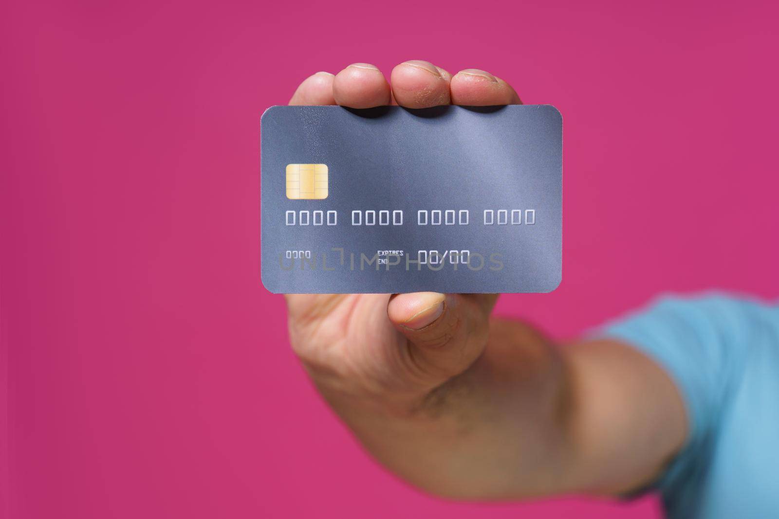 Dark grey-purple debit, credit card in man hand isolated on pink background. Financial, banking concept. No face visible.