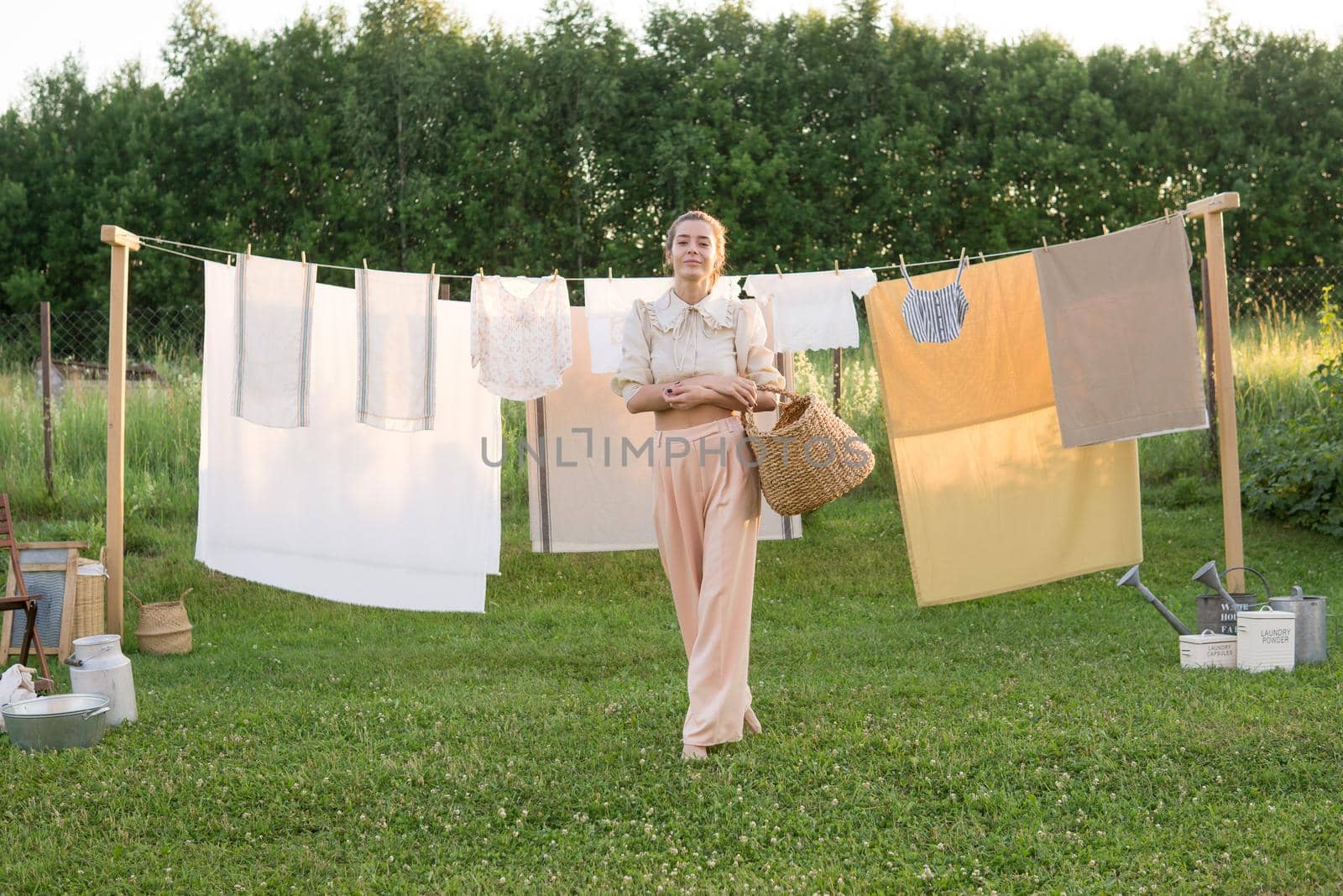Laundry day. A woman hangs linen and towels on a tree in the courtyard of a village house. Summer cottage concept.