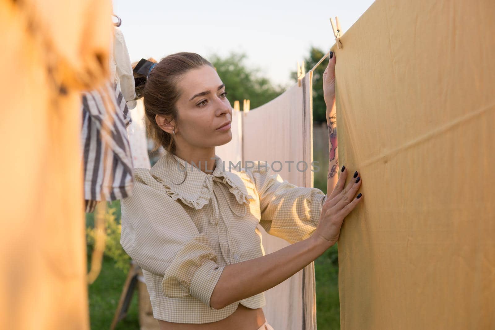 Laundry day. A woman hangs linen and towels on a tree in the courtyard of a village house. Summer cottage concept.
