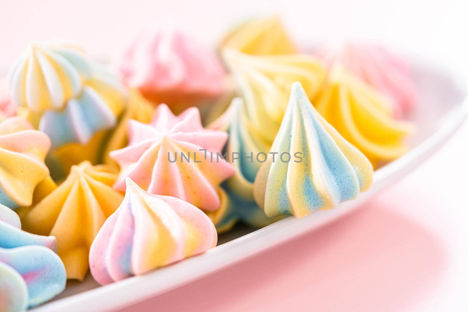 Multicolored unicorn meringue cookies on a white serving plate.