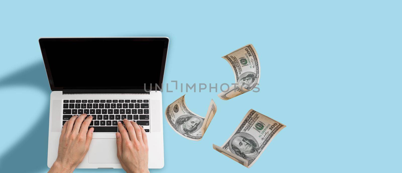 Finance and earning concept, one hundred dollar banknotes flying around laptop, internet, side view on dark background. High quality photo