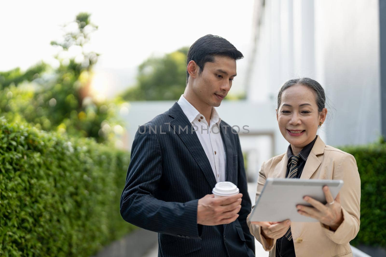 Successful asian businessman and aged businesswoman discussing with tablet outside of the building.