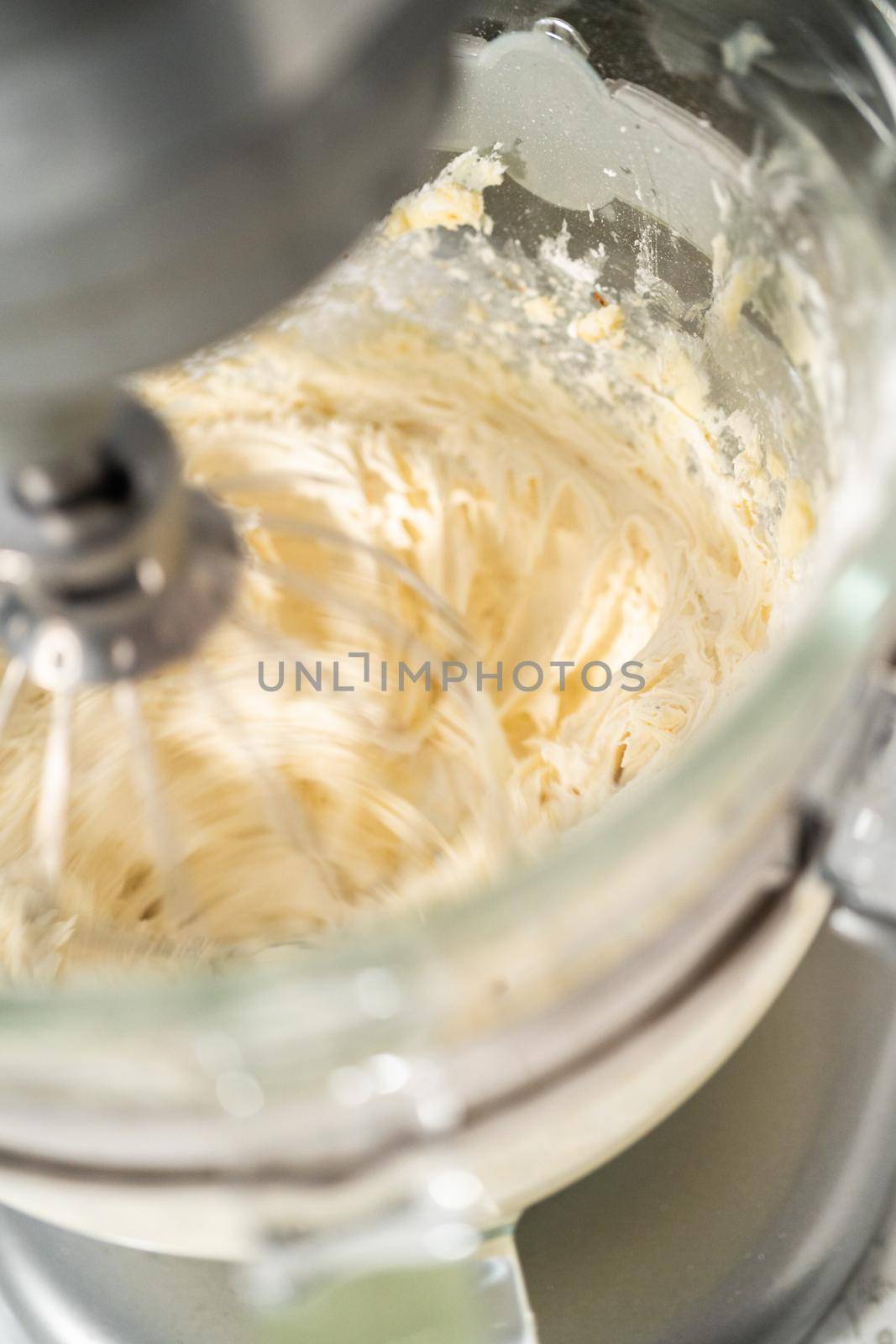 Mixing ingredients in a large glass mixing bowl of kitchen mixer to make eggnog buttercream frosting.