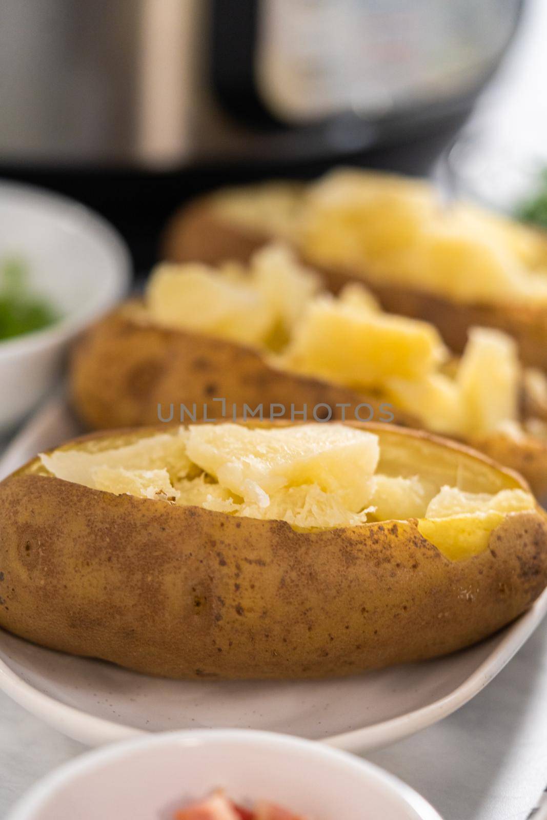 Pressure Cooker Baked Potatoes. Sliced cooked whole potatoes on a white plate to make baked potatoes.