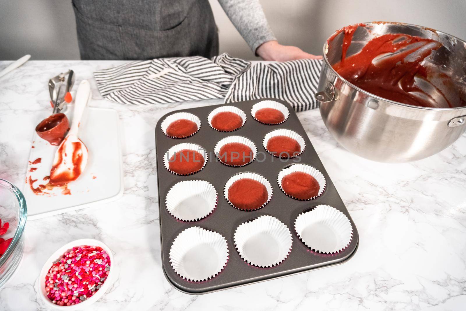 Scooping cupcake batter into a cupcake pan to bake red velvet cupcakes.