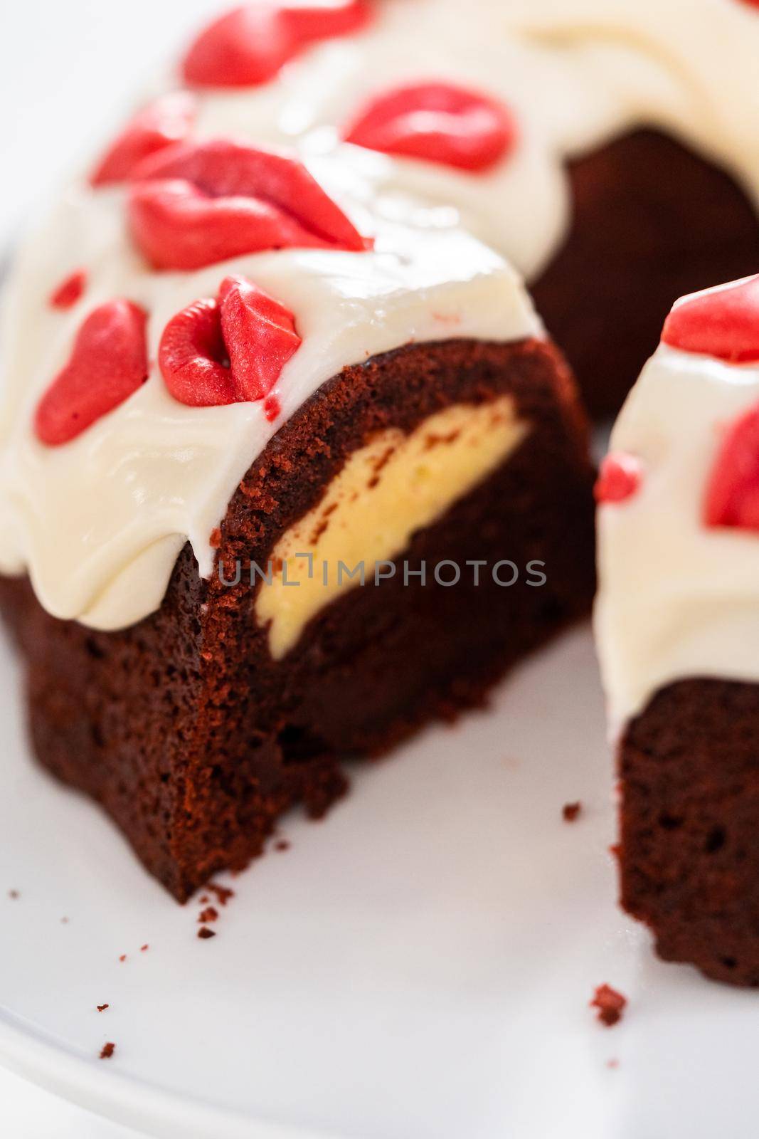 Slicing freshly baked red velvet bundt cake with chocolate lips and hearts over cream cheese glaze for Valentine's Day.