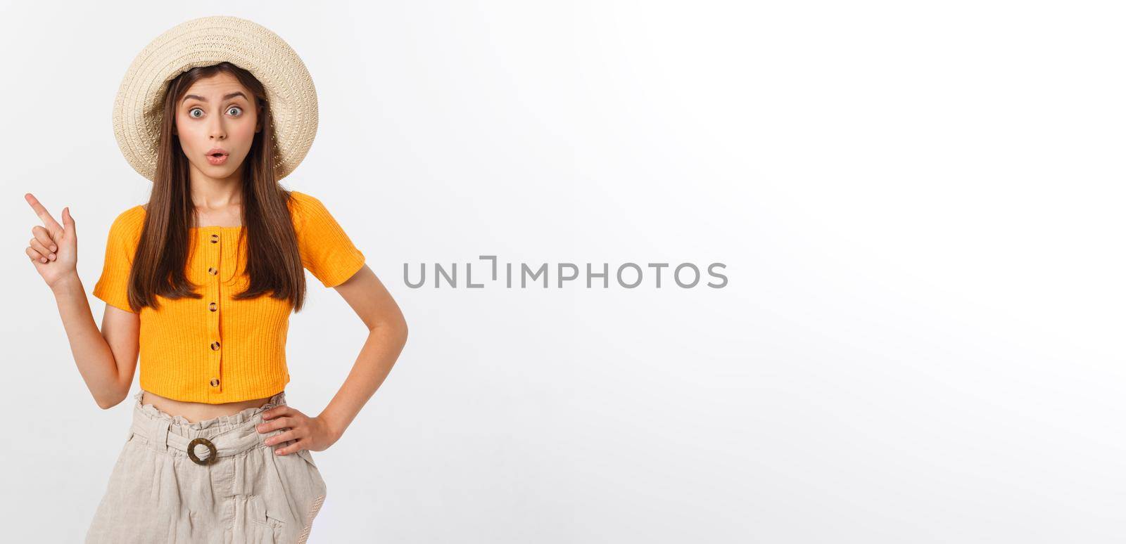 Teenager girl on summer vacation surprised and pointing finger on copy space over isolated white background