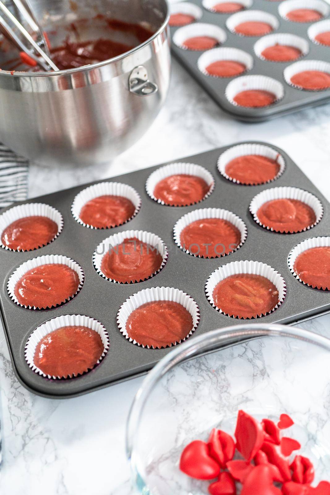 Scooping cupcake batter into a cupcake pan to bake red velvet cupcakes.