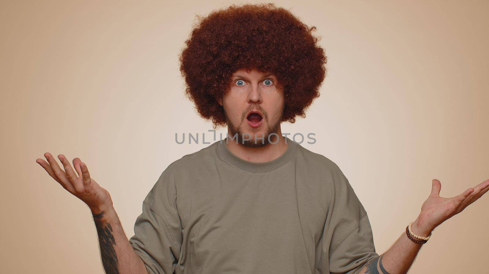 Excited amazed man 30s in t-shirt touching head and showing explosion, looking worried and shocked, professional burnout. Looking surprised wow guy isolated alone on beige studio wall background