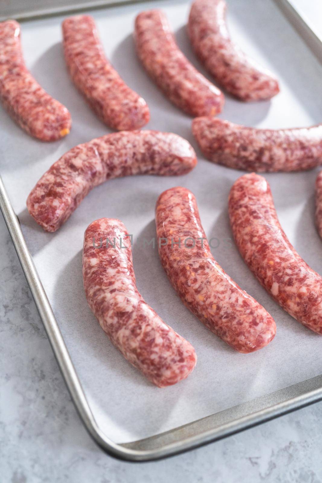 Raw beer bratwursts on a baking sheet lined with parchment paper ready to be cooked in the oven.
