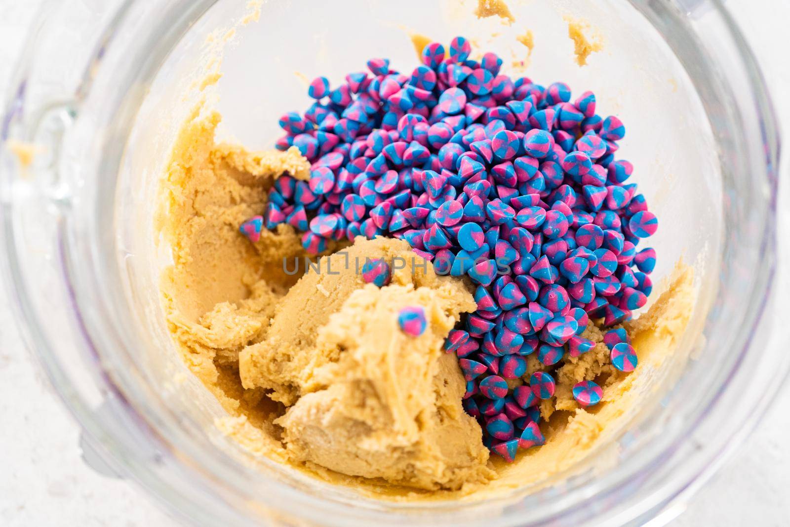 Mixing in rainbow chocolate chips with cookie dough to bake unicorn chocolate chip cookies.