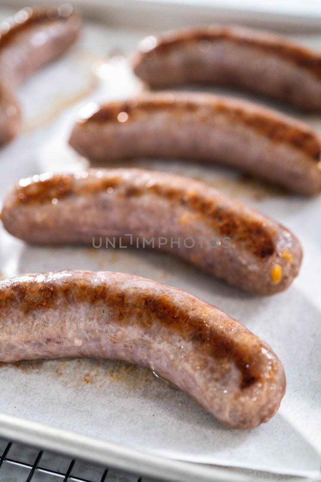 Freshly cooked in oven beer bratwursts on a baking sheet lined with parchment paper.