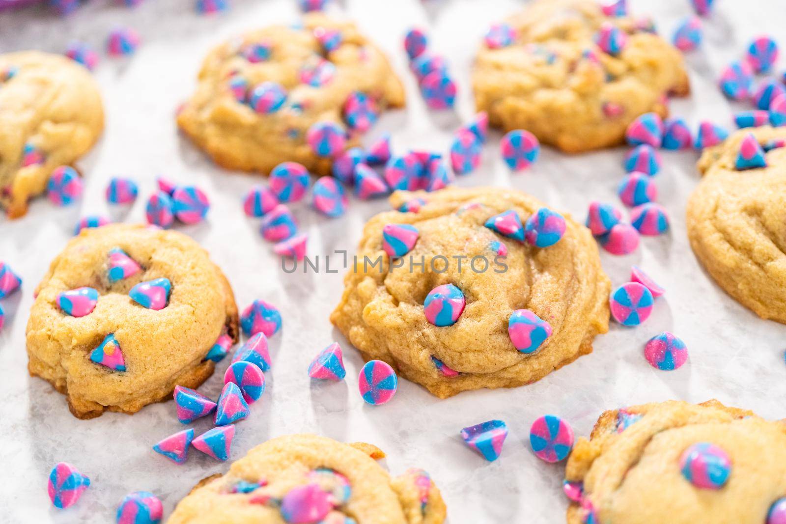 Freshly baked unicorn chocolate chip cookies with rainbow chocolate chips on the counter.