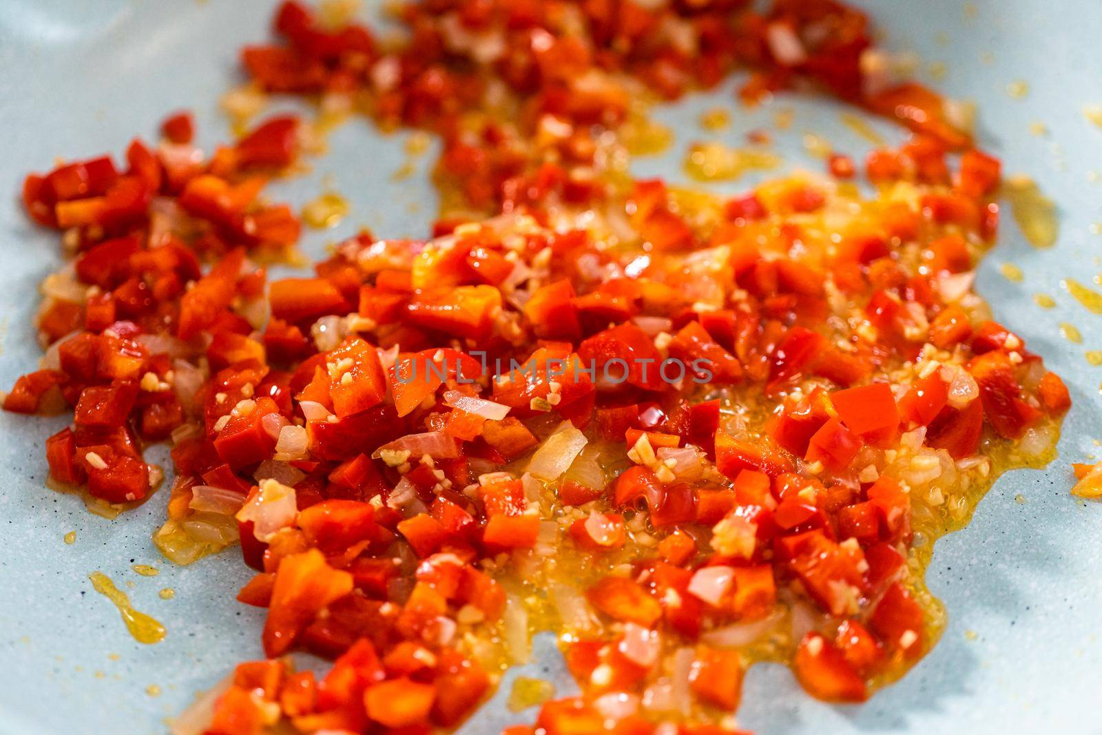 Frying onion and red bell pepper in olive oil on a nonstick frying pan to bake turkey empanadas.